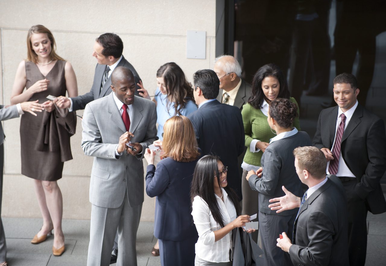 At a networking event, a group of professionals in business attire are mingling, exchanging business cards, and discussing Lorem Ipsum.