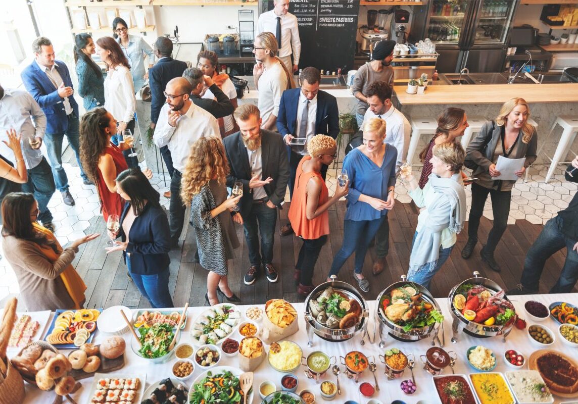 A group of people socializing at a buffet event, surrounded by a variety of dishes.